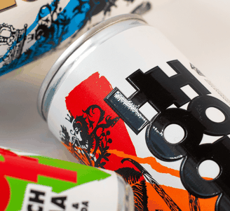 Drie kleurrijke blikjes drank met opvallende, grafische etiketten in rood, oranje, blauw en neonaccenten op een witte achtergrond.