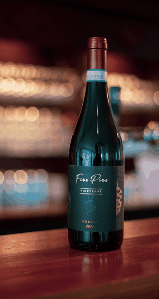 Een donkergroene wijnfles op een houten bar, met zacht vervaagde lichten op de achtergrond.