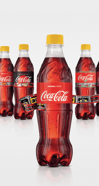 Vijf plastic Coca-Cola-flesjes met gele dopjes en rode etiketten, waarbij het middelste flesje is omwikkeld met een kleurrijk geometrisch patroon, op een witte achtergrond.