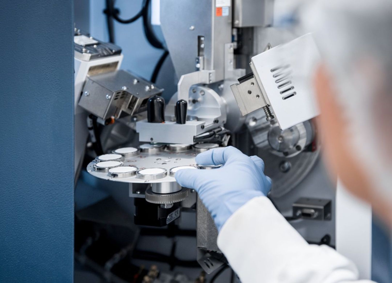 Close-up of a researcher in a lab coat and gloves operating advanced machinery for calcium phosphate analysis at CAM Bioceramics, showcasing innovative bioceramics technology.