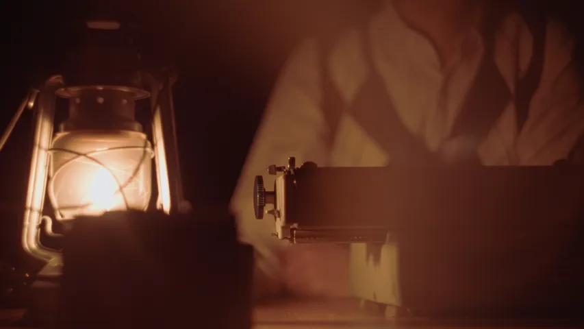 Thumbnail des Projekts «Typewriter» – Bild von einem Mann im Dunkeln, der vor einer Schreibmaschine sitzt und von einer Petrollampe erleuchet wird.