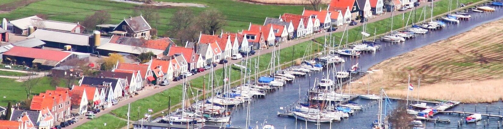 luchtfoto van Durgerdam met bootjes voor de straat en rode daken. De velden zijn zichtbaar achter de huisjes