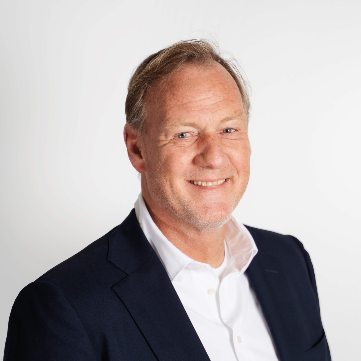 foto van een blanke man met witte blouse en jasje. hij lacht naar de camera