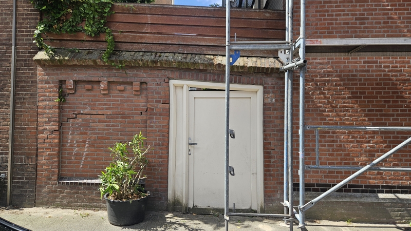 foto van een muur met verzakkingen erin. De deur is scheef en in de muur zijn duidelijke scheuren te zien