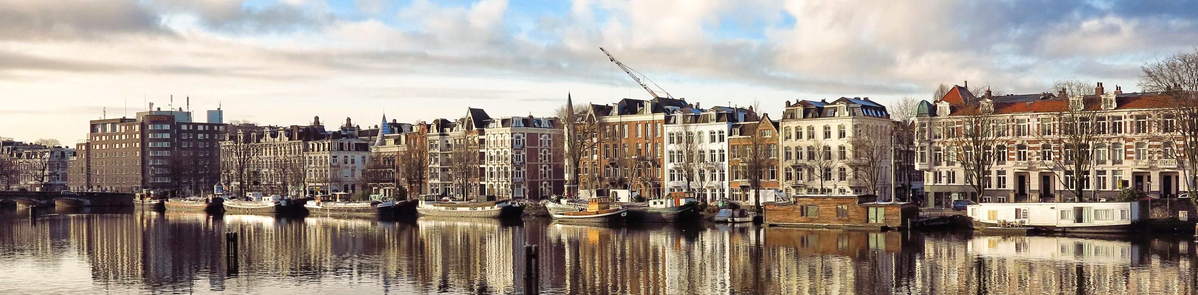 Foto van de Weesperzijde vanaf de Amsteldijk, pandjes langs het water