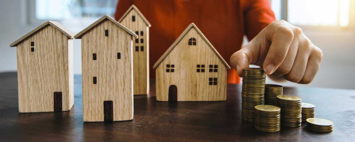 Tafel met houten huisjes en een stapel munten, een hand verplaatst een munt naar een andere stapel