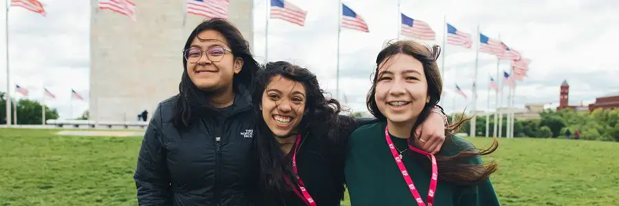 Three travelers smiling in front of the Washington Monument