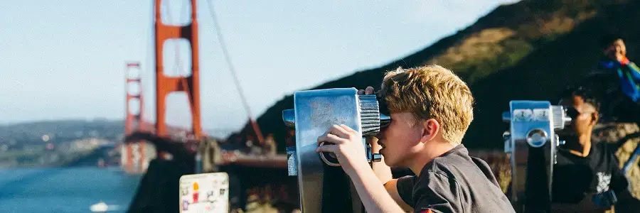 Student traveler looking through a viewing telescope near the Golden Gate Bridge