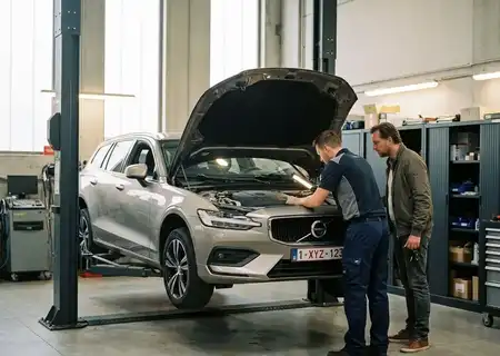 Mechanieker controleert met een zaklamp de motor van een grijze break op de brug in de werkplaats, terwijl de eigenaar meekijkt tijdens het onderhoud