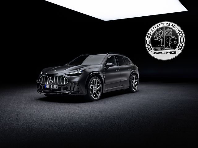 A sleek black Mercedes-AMG SUV with a shiny grille is in a dark room featuring a large illuminated logo on the wall, showcasing a luxury car brand.