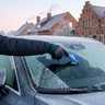 Man krabt op een ijzige winterochtend de bevroren voorruit van zijn auto vrij in een Vlaamse dorpsstraat