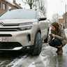 Vrouw controleert met een zaklamp de profieldiepte van de winterbanden van haar Citroën C5 Aircross in een besneeuwde straat