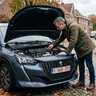 Man controleert de batterijklemmen onder de open motorkap van zijn Peugeot 208 die niet wil starten
