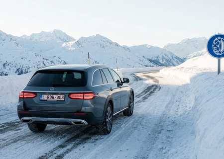 Mercedes-Benz E-Klasse All-Terrain op een besneeuwde bergweg in de Alpen naast een verkeersbord voor verplichte sneeuwkettingen