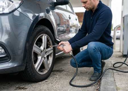 Man pompt de band van zijn auto op aan het bandenpomptoestel van een tankstation na een waarschuwing van het bandenspanning lampje