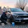 Man controleert de bandenspanning van zijn Kia Sportage op een ijzige winterochtend in een Vlaamse dorpsstraat
