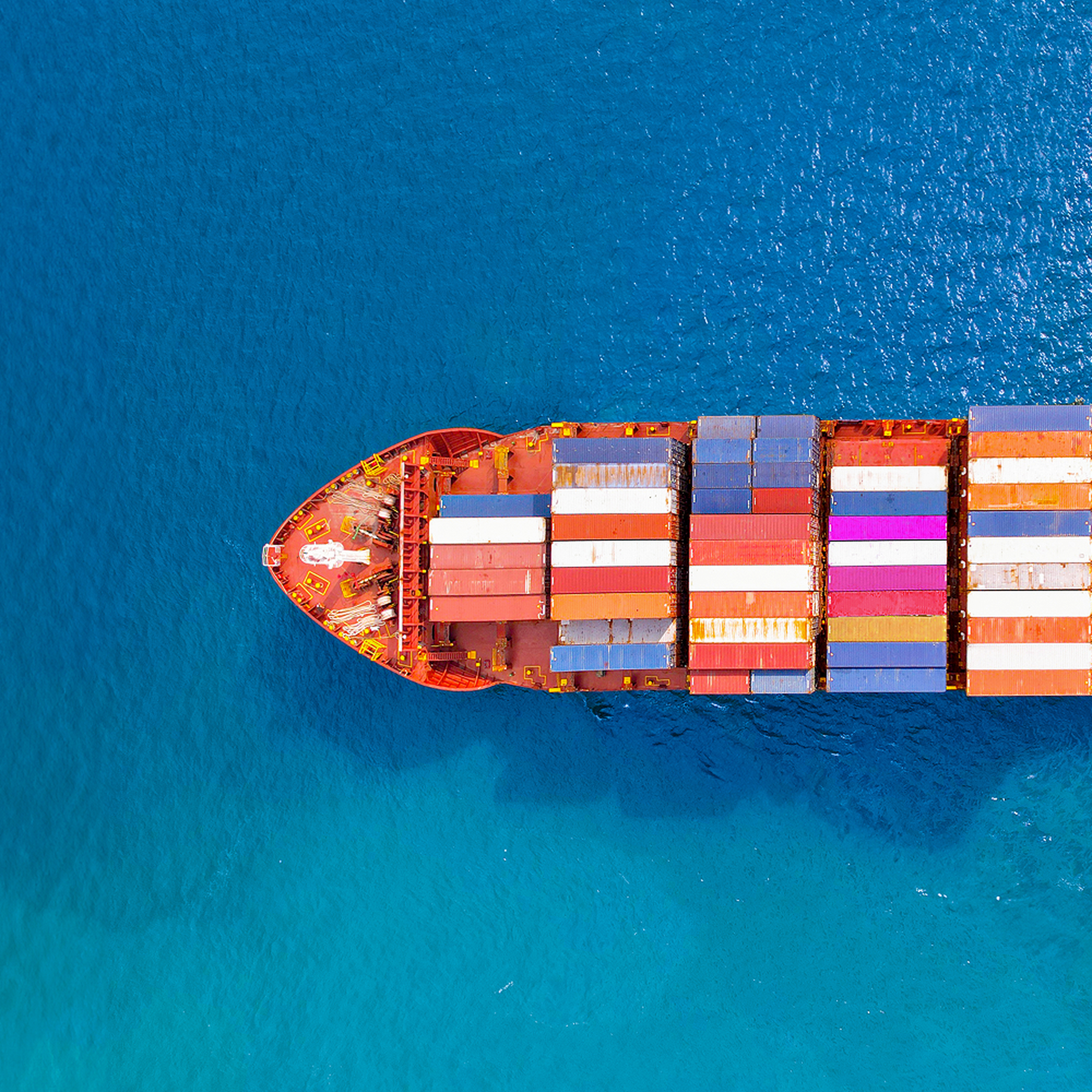 Aerial view of a cargo ship with colorful containers sailing in deep blue water.