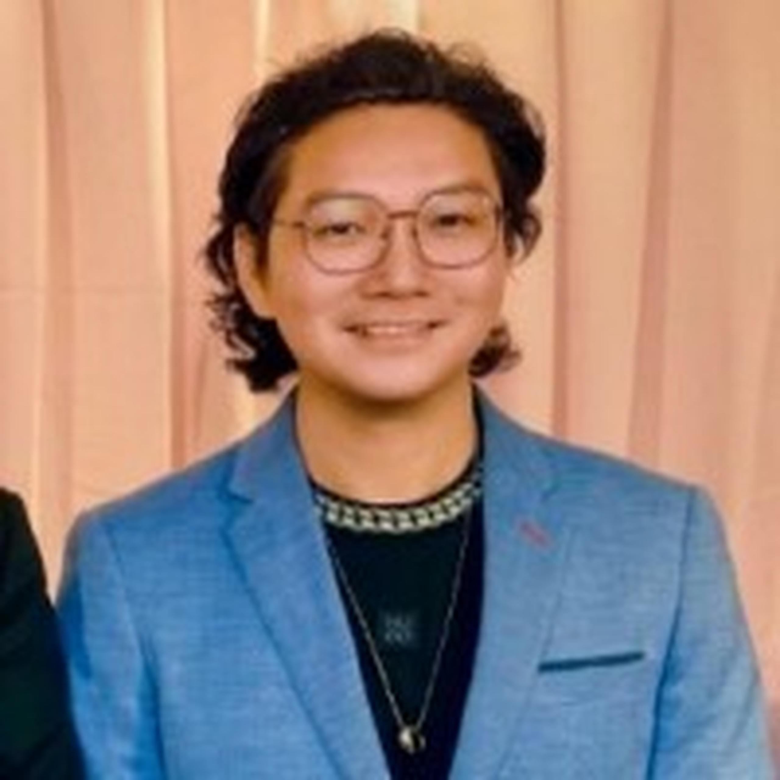 Smiling man, weavy hair, wearing glasses and a blazer
