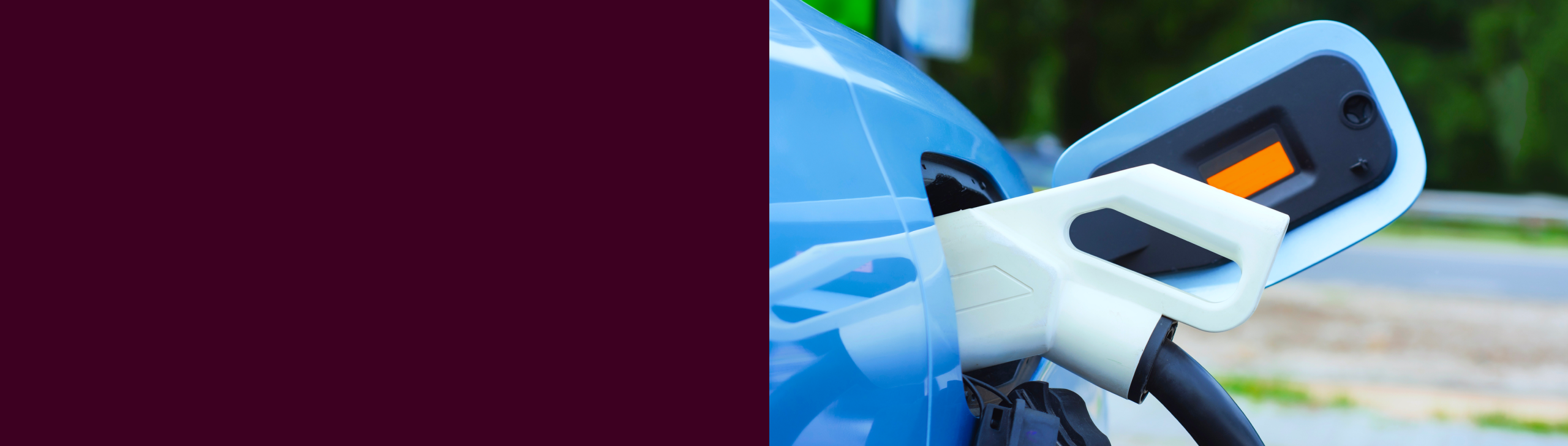 Close-up of an electric vehicle being charged, with the charging cable connected to a blue car against a blurred outdoor background.