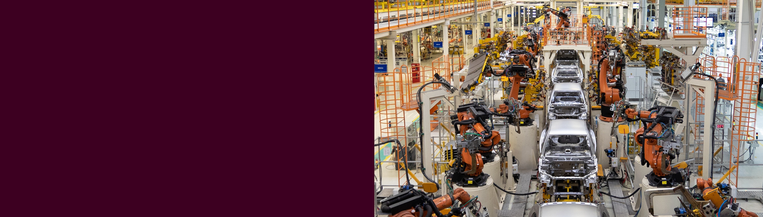 A car manufacturing assembly line with robotic arms working on vehicle frames in a factory setting.