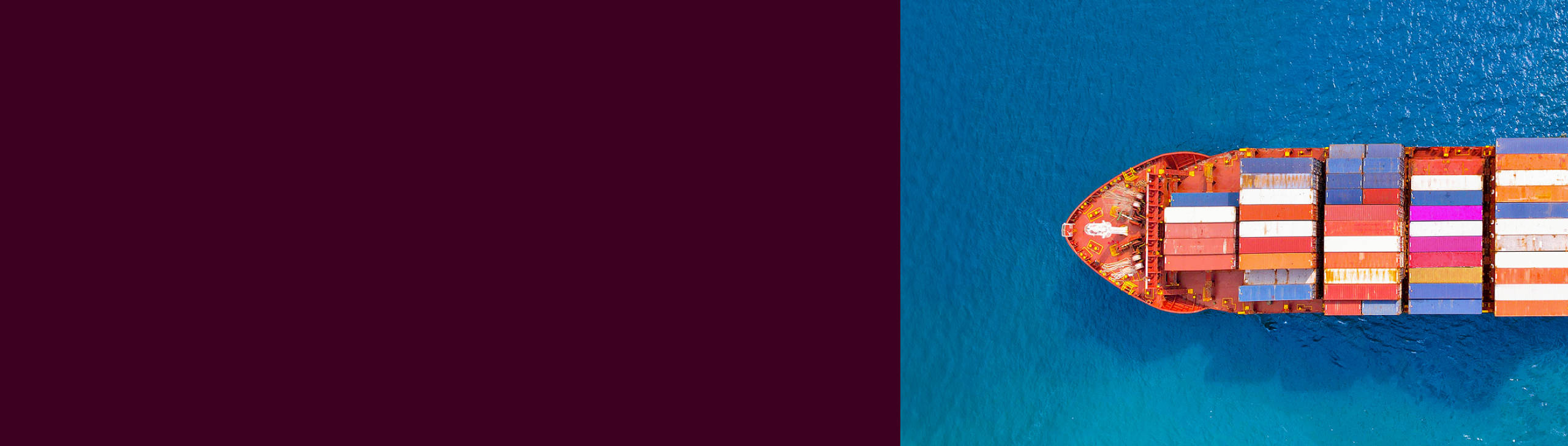 Top view of a red cargo ship with colorful containers in blue ocean water, with a maroon divider on the left.