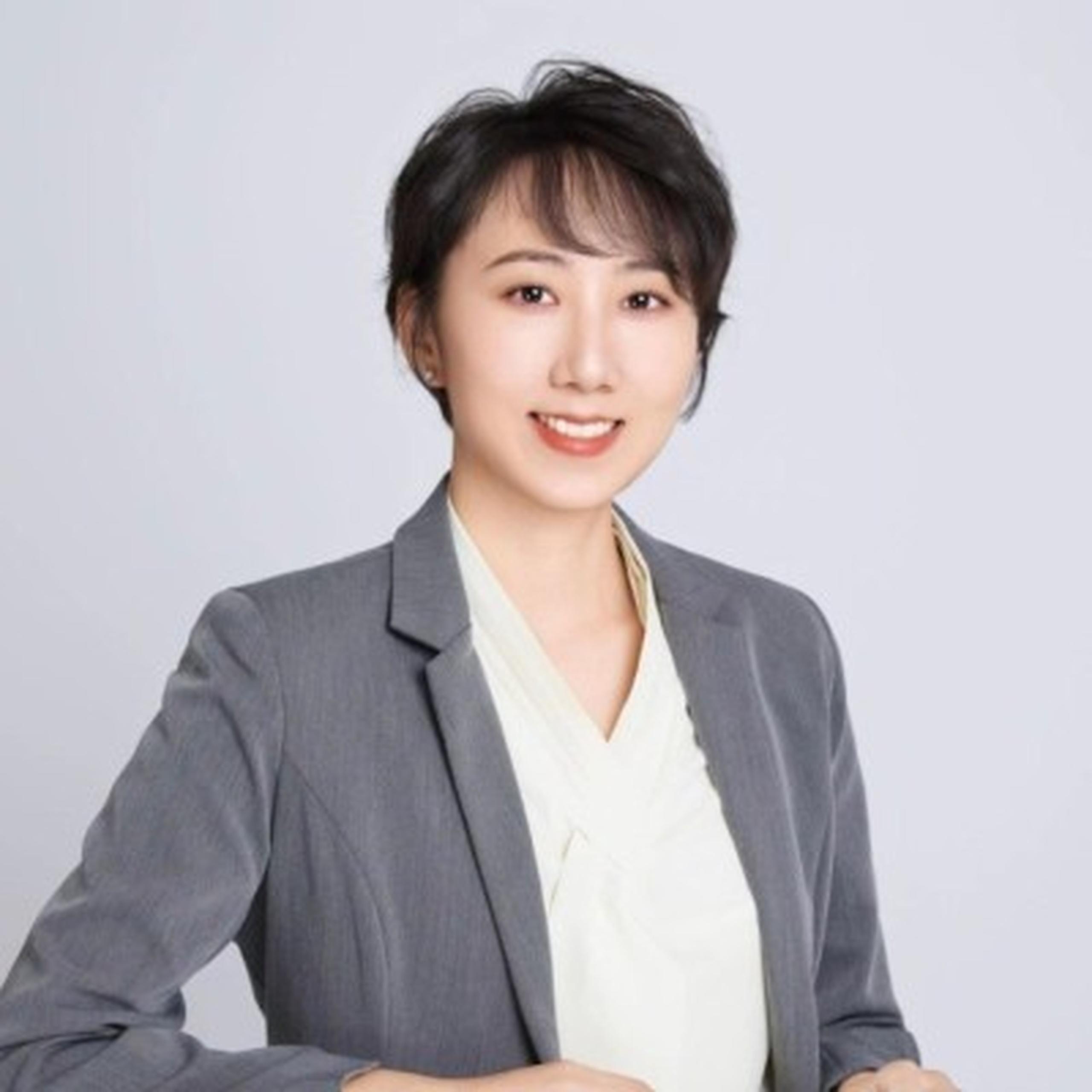 A person with short dark hair in a gray blazer and white blouse, smiling against a plain background.