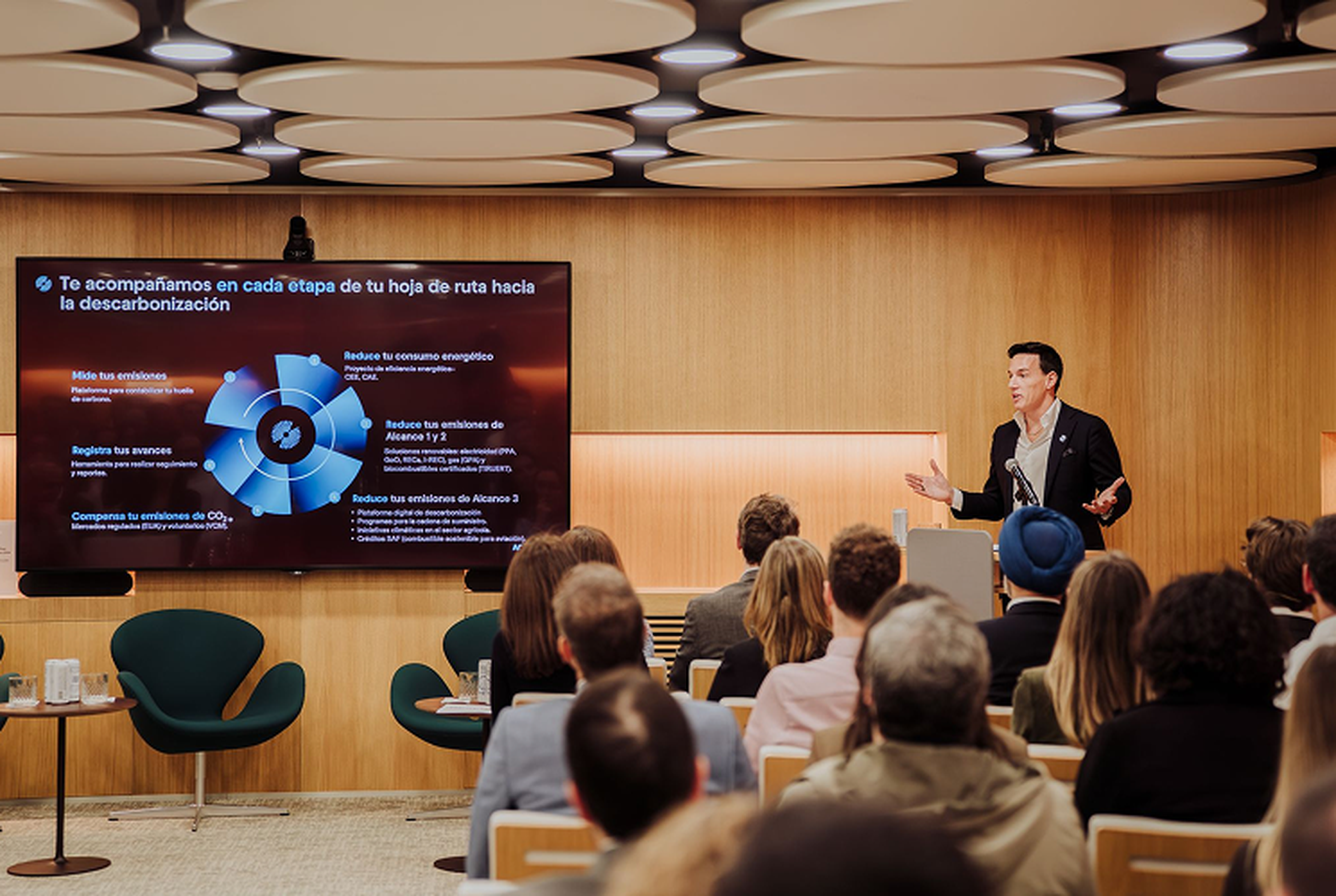 A speaker from ACT addresses an audience in a modern conference room, presenting a slide on decarbonization strategies.