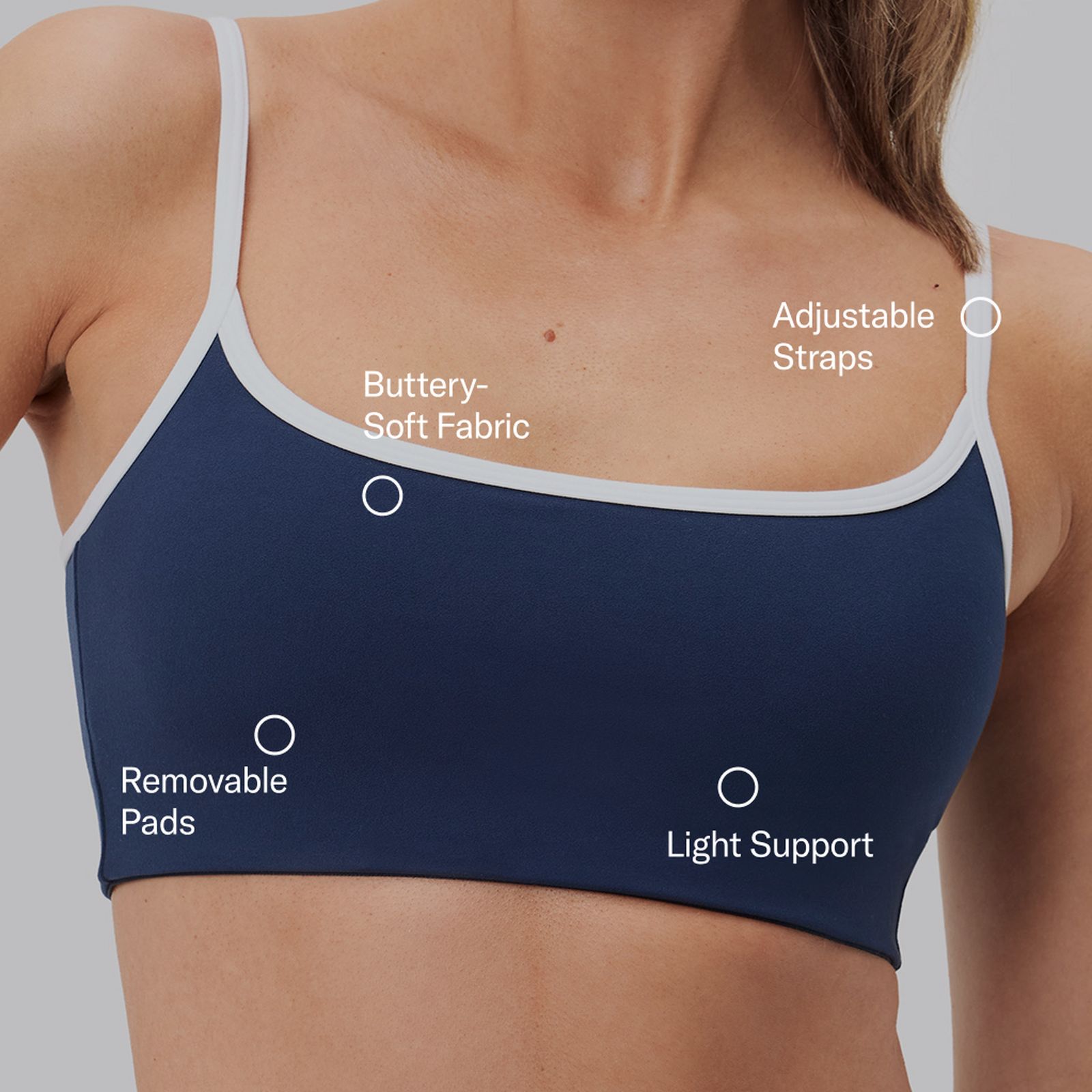 Close-up of a navy sports bra with white trim, featuring adjustable straps, buttery-soft fabric, removable pads, and light support.