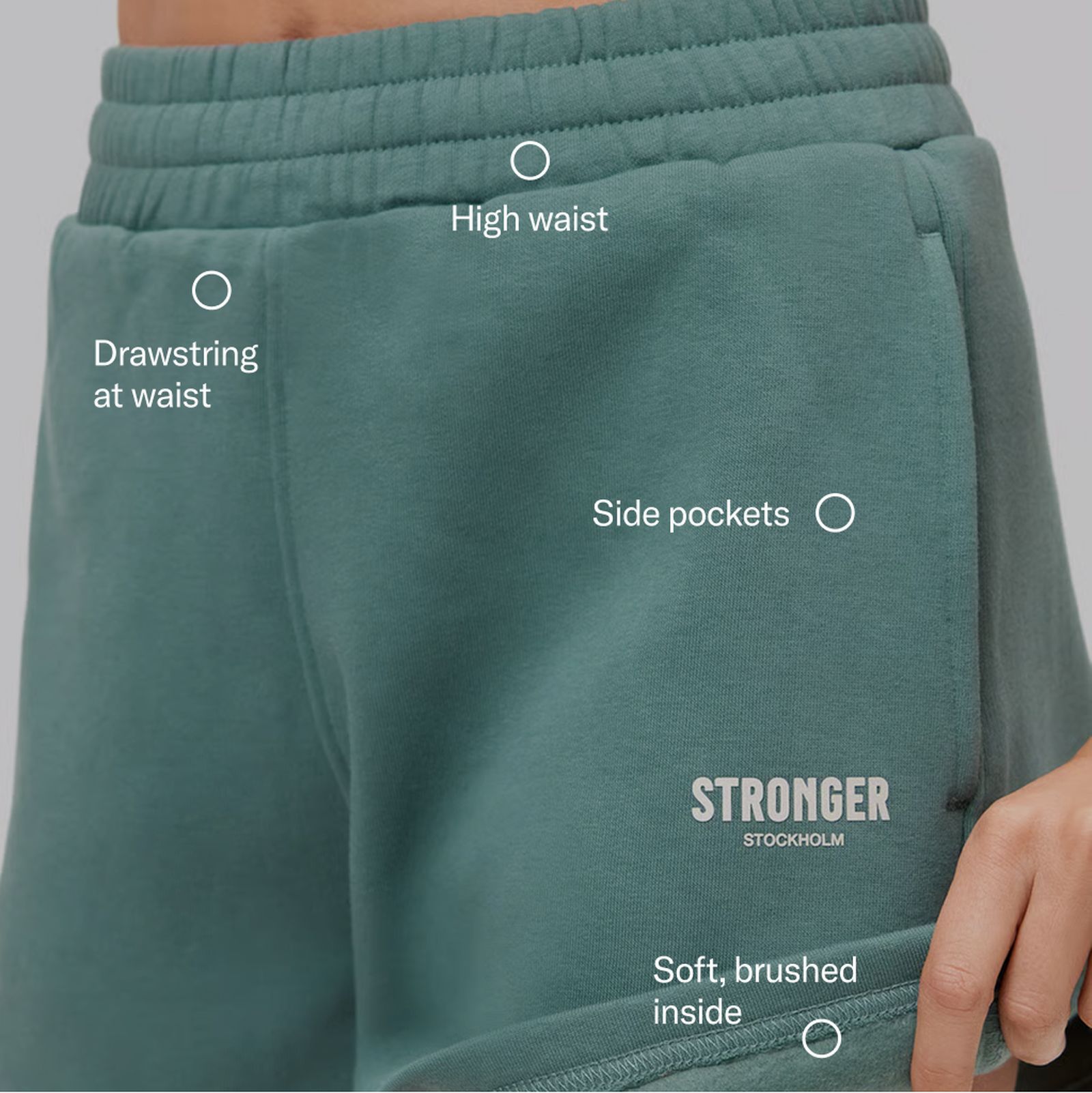 Close-up of teal shorts featuring a high waist, drawstring, side pockets, soft brushed inside, and "Stronger Stockholm" logo.