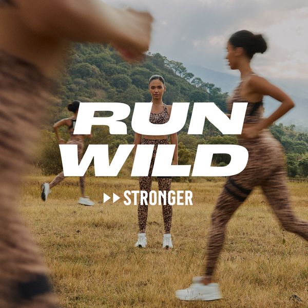 Women in leopard-print activewear run in a field with "Run Wild Stronger" text overlay. Lush greenery and hills in the background.