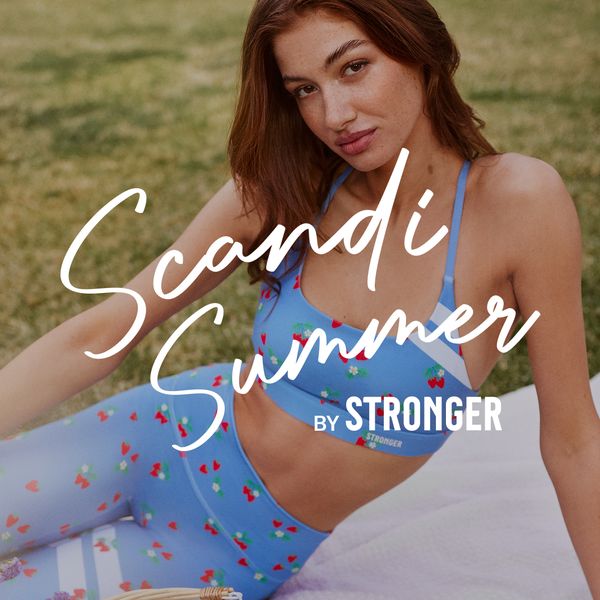 Woman in blue athletic wear with cherry patterns, sitting on grass. Text reads, "Scandi Summer by Stronger."