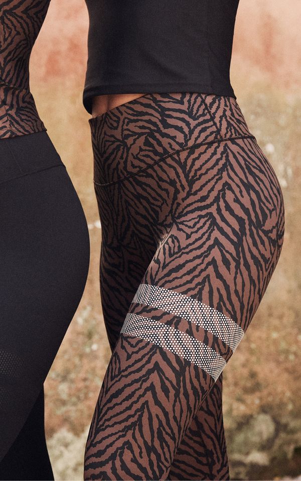 A person wearing black and brown zebra-patterned leggings with a decorative band. They are standing sideways against a blurred background.