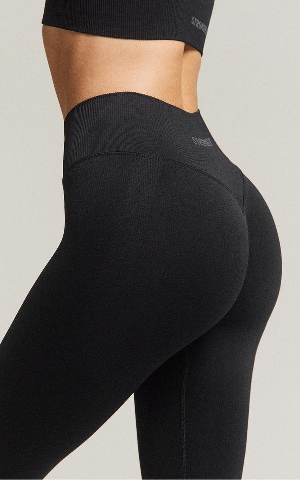 Person wearing black, high-waisted leggings and a matching crop top, showcasing a seamless design against a neutral background.