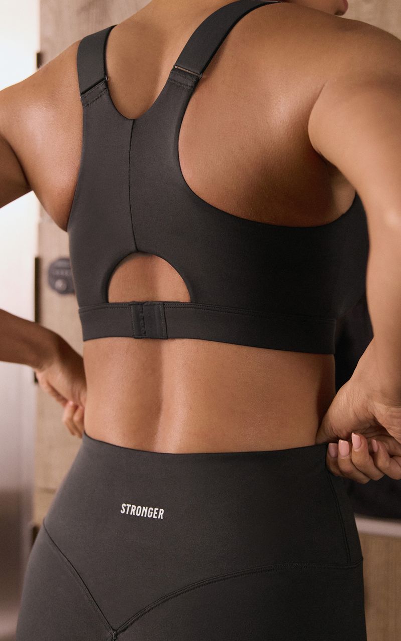 Person wearing a black sports bra and leggings with "STRONGER" written on the waistband, adjusting the leggings in a room.