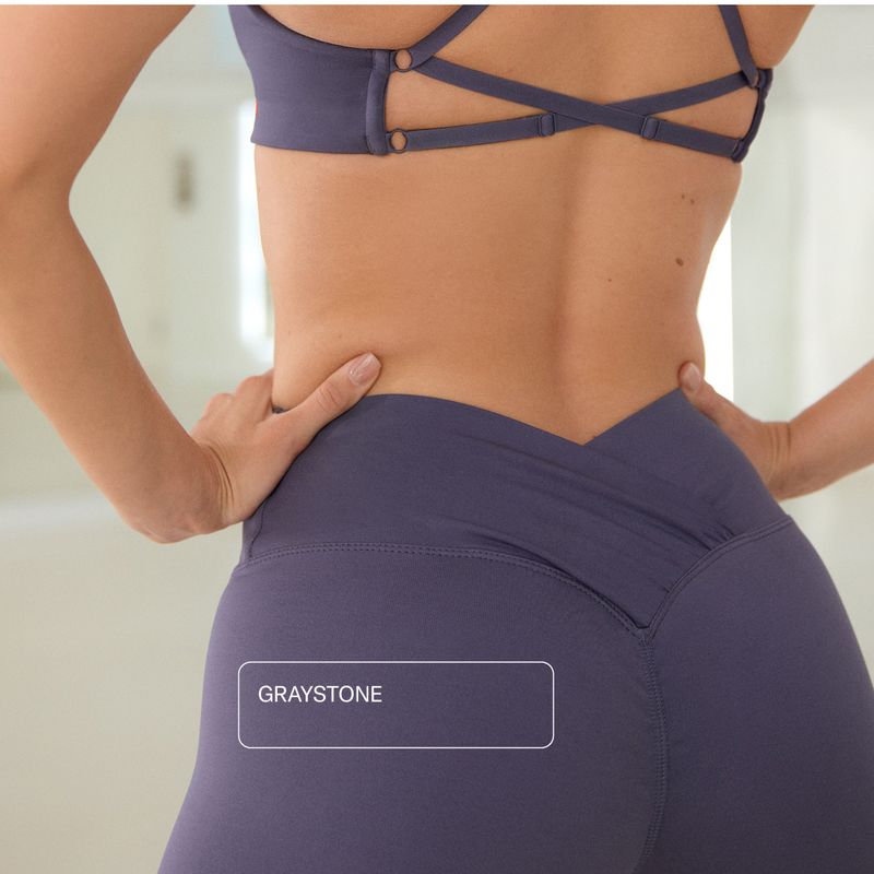 Person in a strappy sports bra and high-waisted leggings with hands on hips, in a bright room. Text reads "GRAYSTONE."