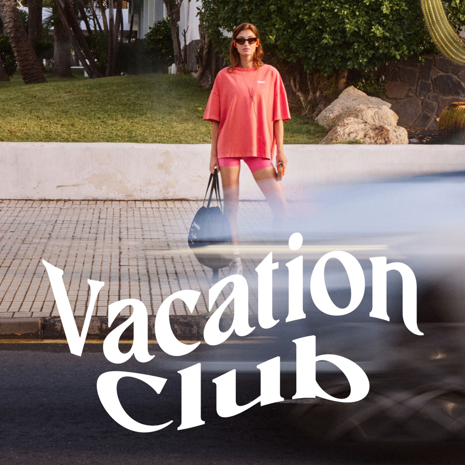 A person in a pink outfit stands on a sidewalk, holding a bag, with blurred traffic in the foreground and "Vacation Club" text overlaid.