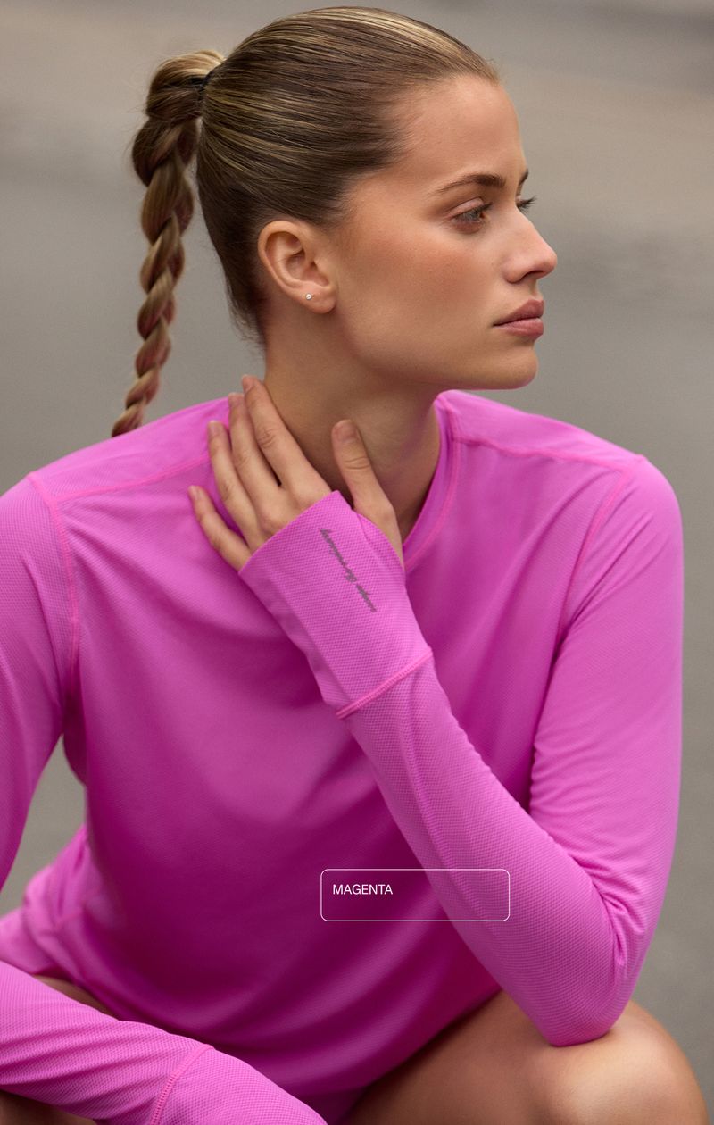 Woman in a pink long-sleeve shirt with braided hair, sitting outdoors, looking to the side.