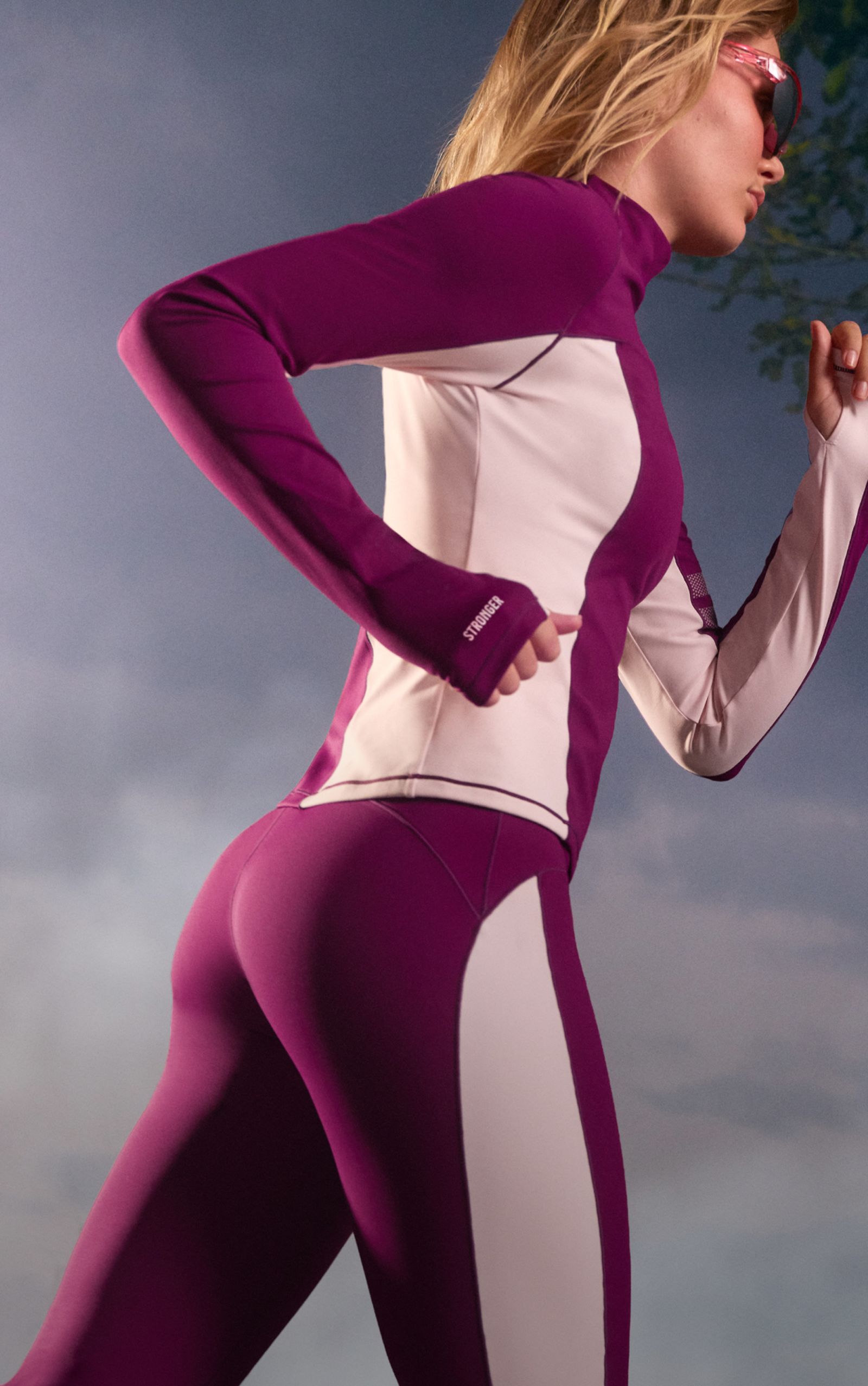 Person jogging in a purple and white athletic outfit, wearing sunglasses, against a cloudy sky background.
