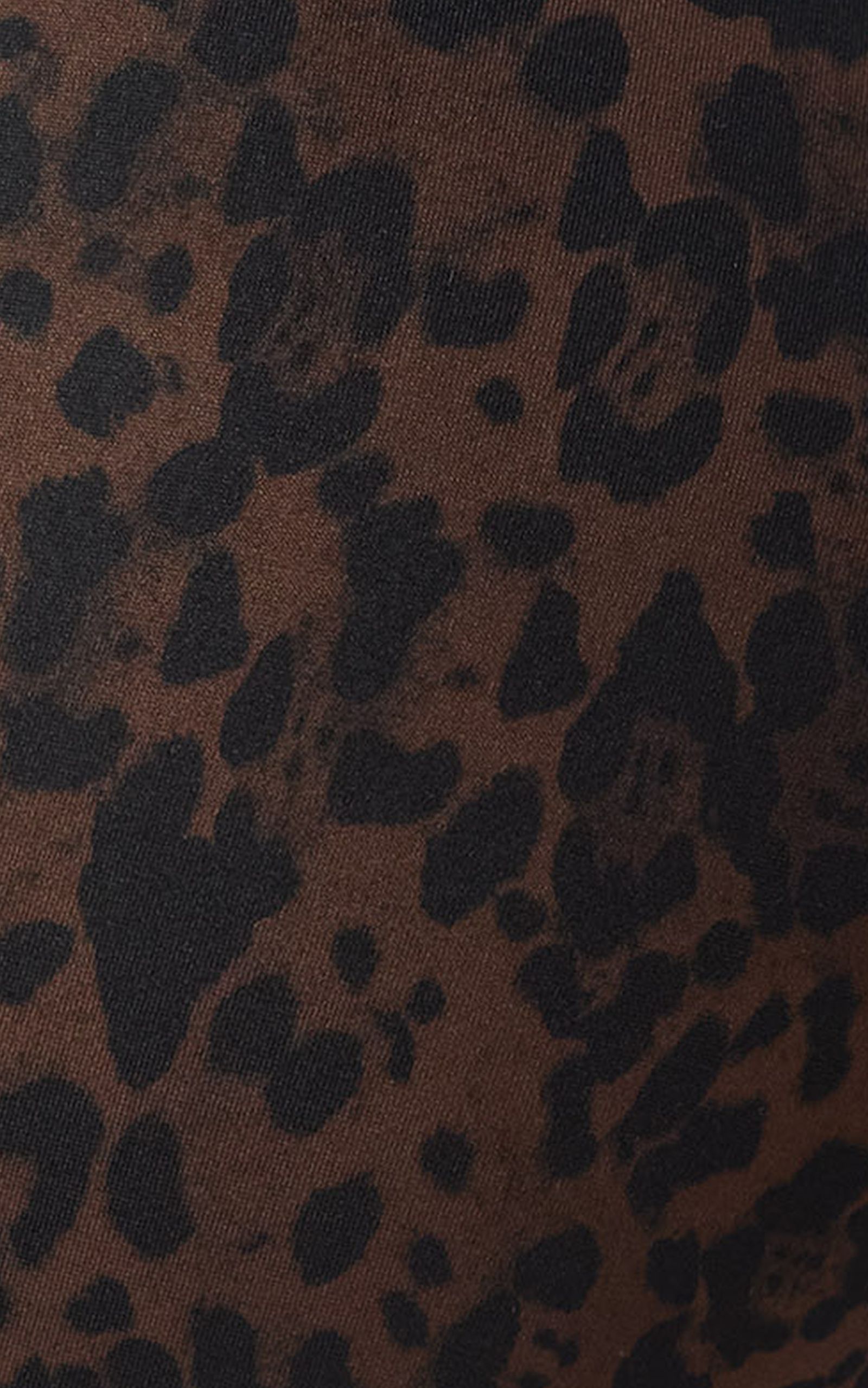 Close-up of a fabric with a brown and black leopard print pattern, showcasing irregular dark spots on a textured surface.