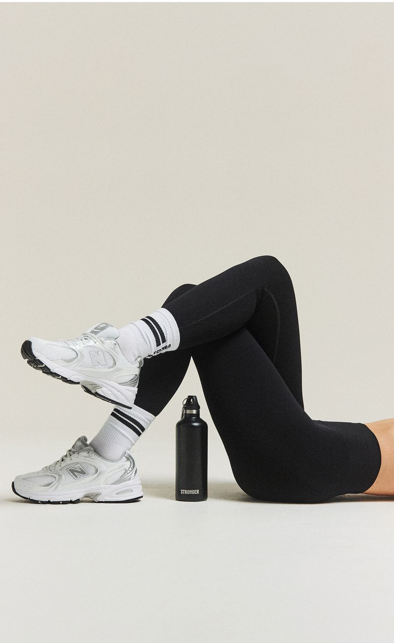 Person in black leggings and white sneakers lying on their back with legs crossed, next to a black water bottle.