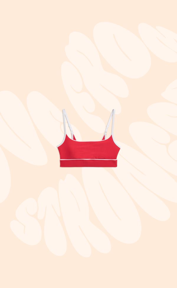 Red sports bra with white trim on a beige background with abstract white lettering.