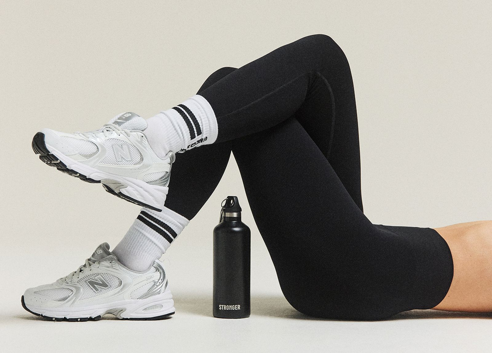 Person wearing black leggings and white sneakers with striped socks, lying on their back, with a black water bottle nearby.