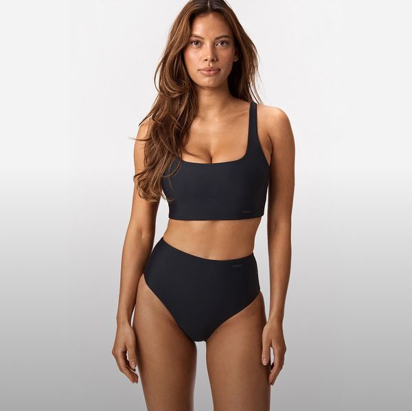 Woman with long hair wearing a black two-piece swimsuit, standing against a white background.