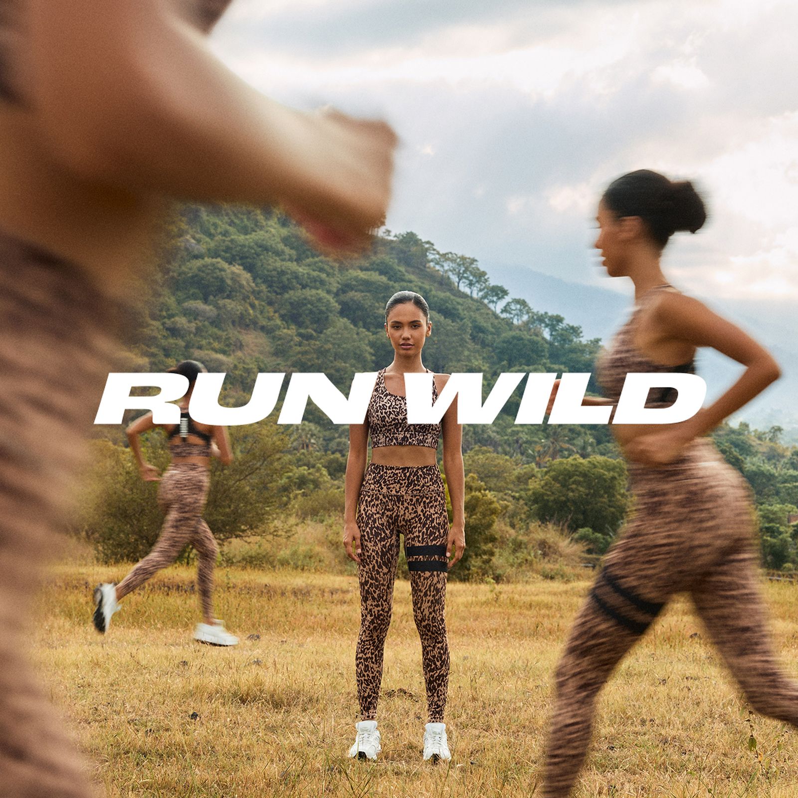 Women in leopard-print workout gear run through a grassy field with mountains in the background. Text: "RUN WILD."