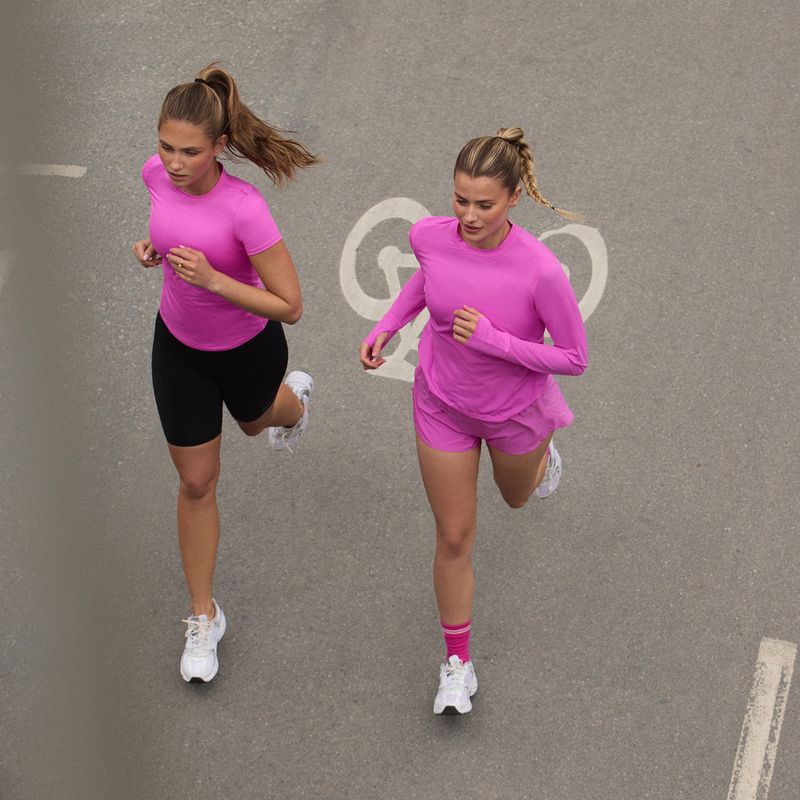 Two women in pink athletic wear jogging on a paved path, viewed from above.