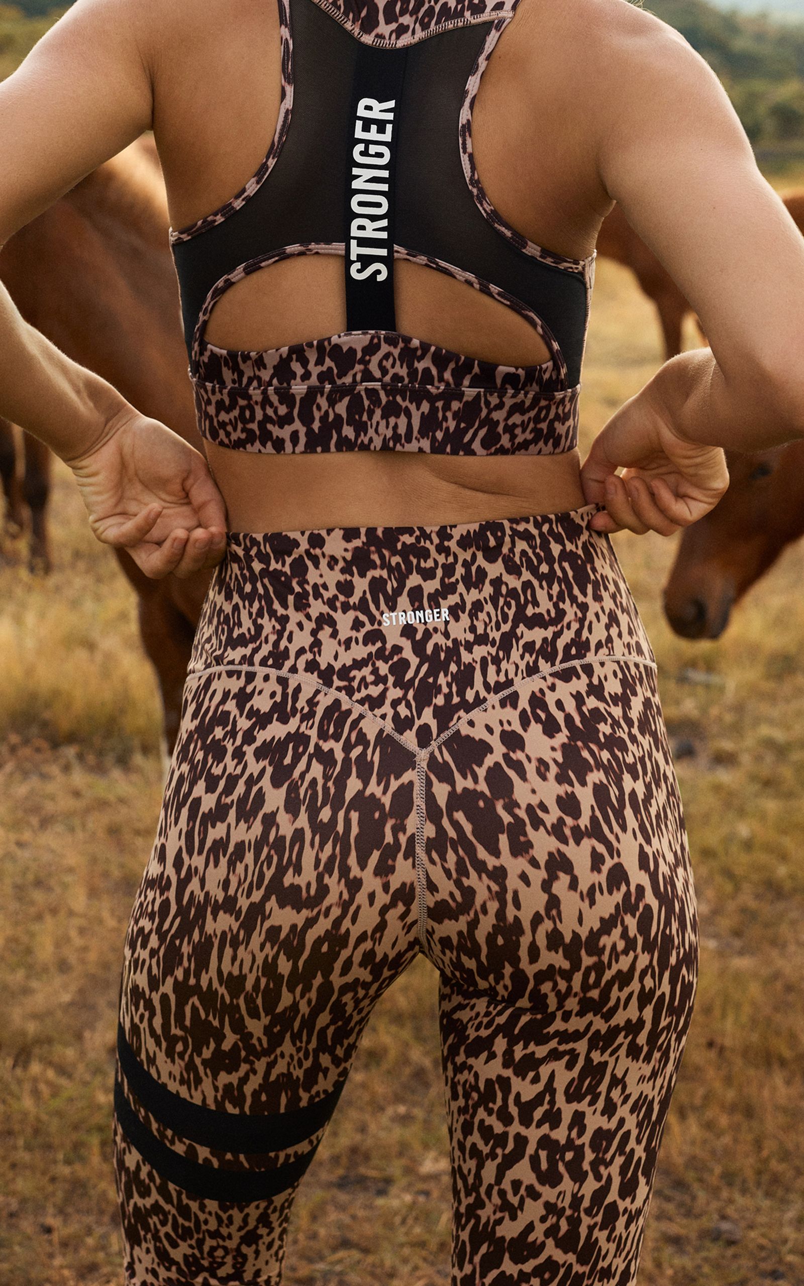 Woman in leopard print athletic wear with "STRONGER" text stands outdoors, adjusting waistband.
