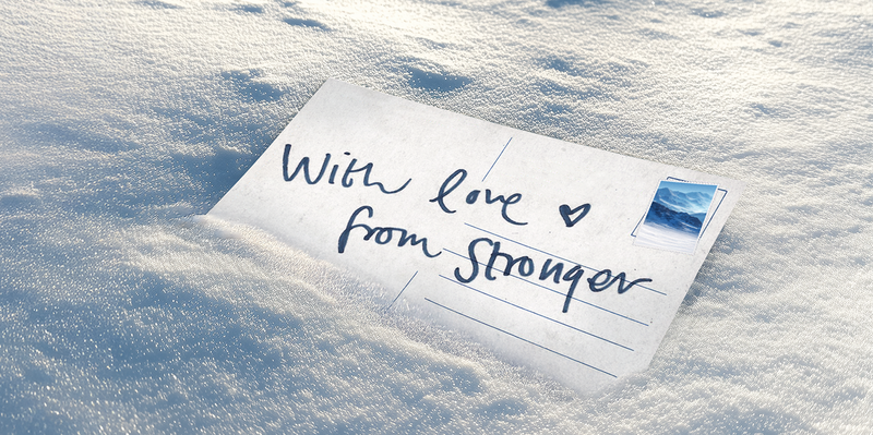 A postcard partially buried in snow reads "With love ♥ from Stronger" with a blue stamp in the corner.