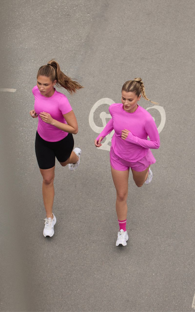 Two women in pink athletic outfits jogging on a paved path with a bicycle symbol.