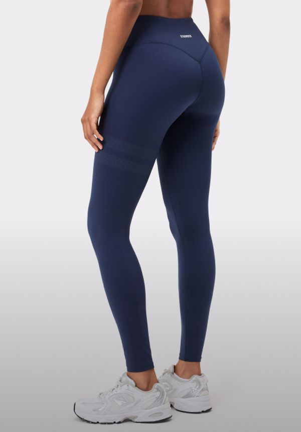 Person in navy leggings and white sneakers is standing sideways, showcasing the back design of the outfit on a plain background.