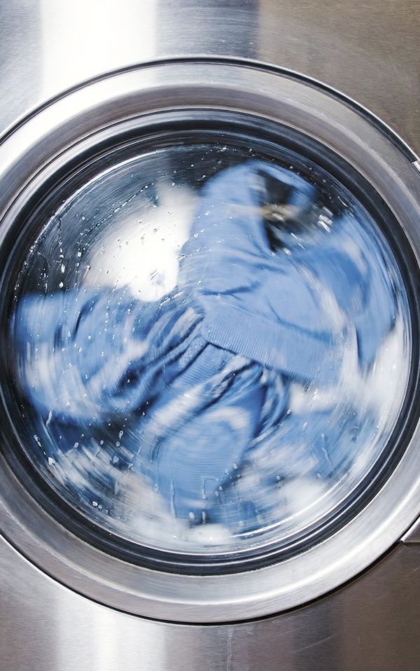 Blue clothes spinning inside a front-loading washing machine, surrounded by soap suds on the glass door.